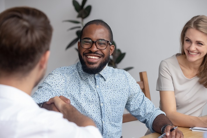 Three people sat around a desk, smiling, two are shaking hands